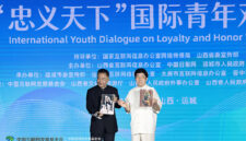 Li Zijun (right), a scholar of the Chinese Theatre Literature Society, displays a photo of his grandfather, Li Hongchun, portraying the legendary Chinese figure Guan Gong during the International Youth Dialogue on Loyalty and Honor Without Borders in Yuncheng, Shanxi province, on Wednesday. [Photo by Zhu Xingxin/China Daily]