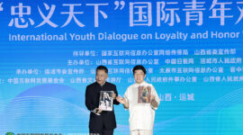 Li Zijun (right), a scholar of the Chinese Theatre Literature Society, displays a photo of his grandfather, Li Hongchun, portraying the legendary Chinese figure Guan Gong during the International Youth Dialogue on Loyalty and Honor Without Borders in Yuncheng, Shanxi province, on Wednesday. [Photo by Zhu Xingxin/China Daily]